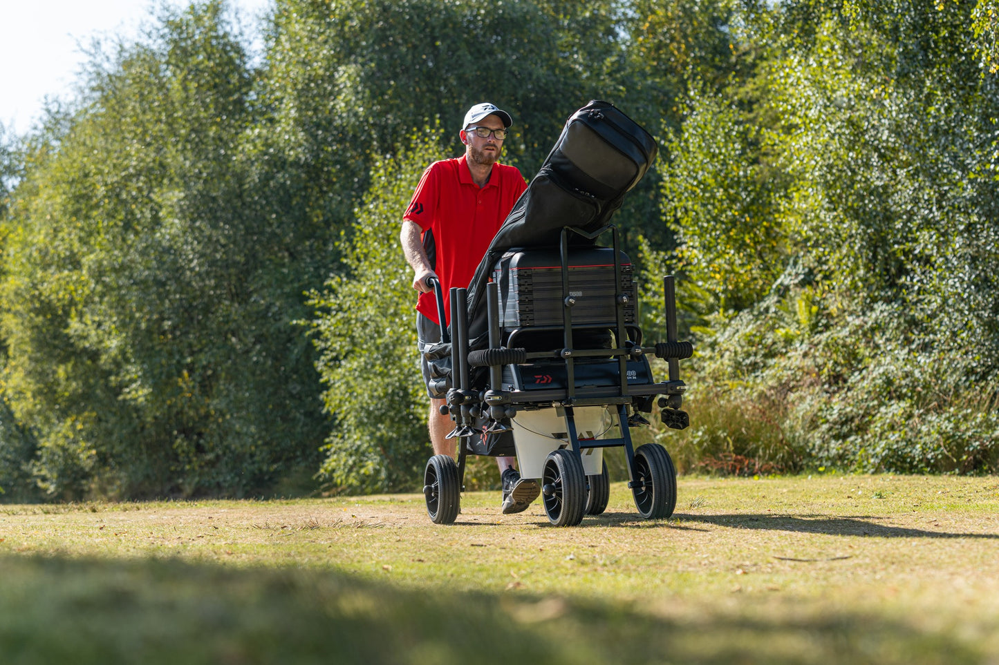 Рибар носи количка за багаж Daiwa DAIWA FOLD N GO MATCH BARROW на риболовно място в природата.