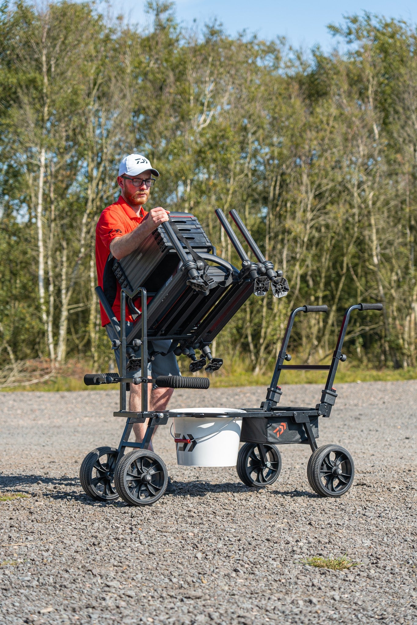Мъж поставя риболовни такъми на количка за багаж Daiwa DAIWA FOLD N GO MATCH BARROW на открито.