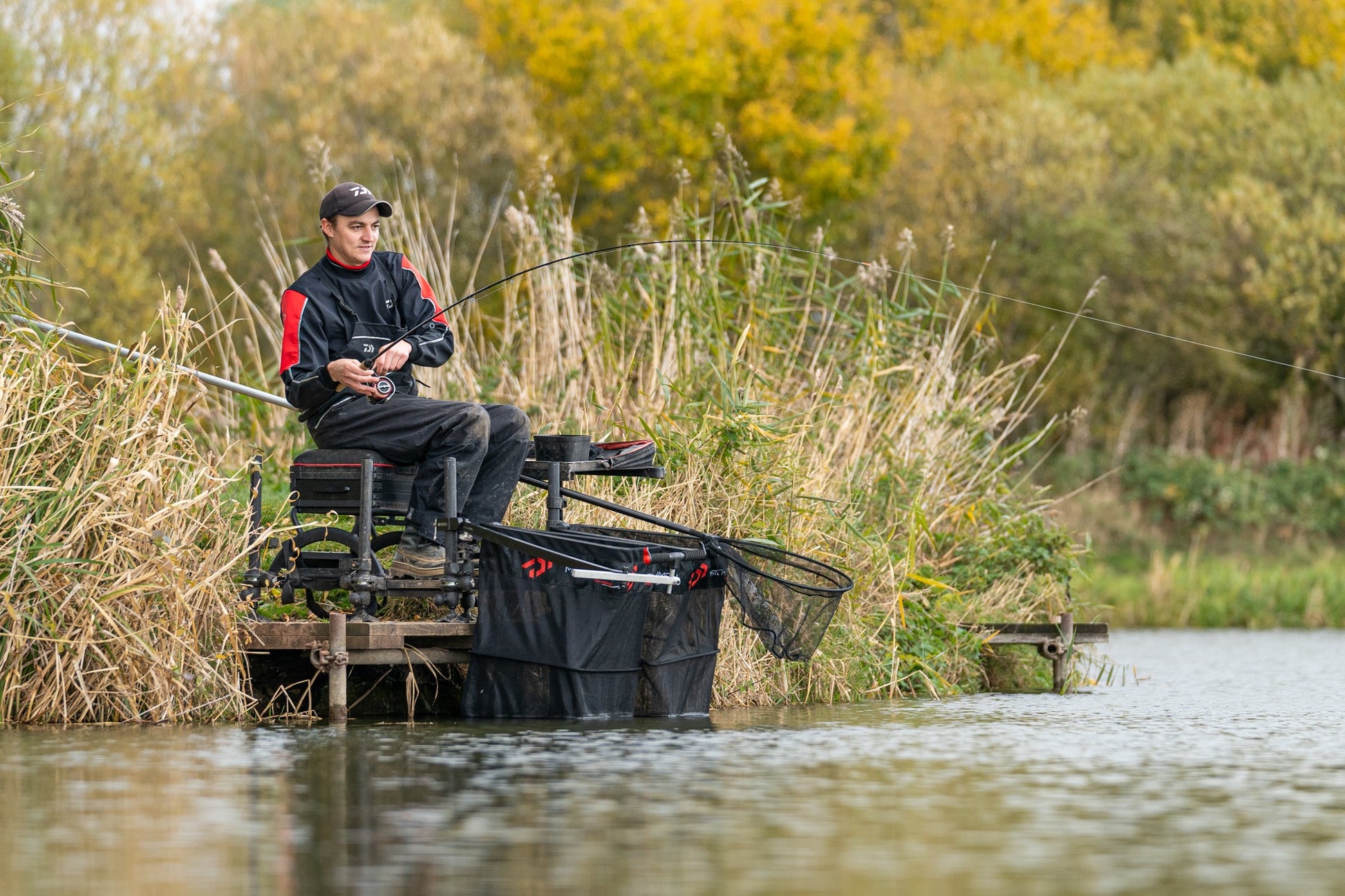 Риболов на платформата DAIWA D500SB - D36 в природата, рибар с въдица край водата и храстите.
