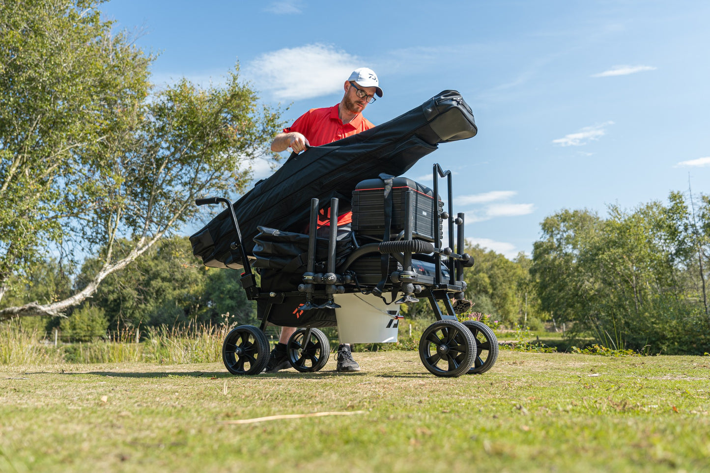 Количка за багаж Daiwa DAIWA FOLD N GO MATCH BARROW, използвана от рибар на зелено поле.