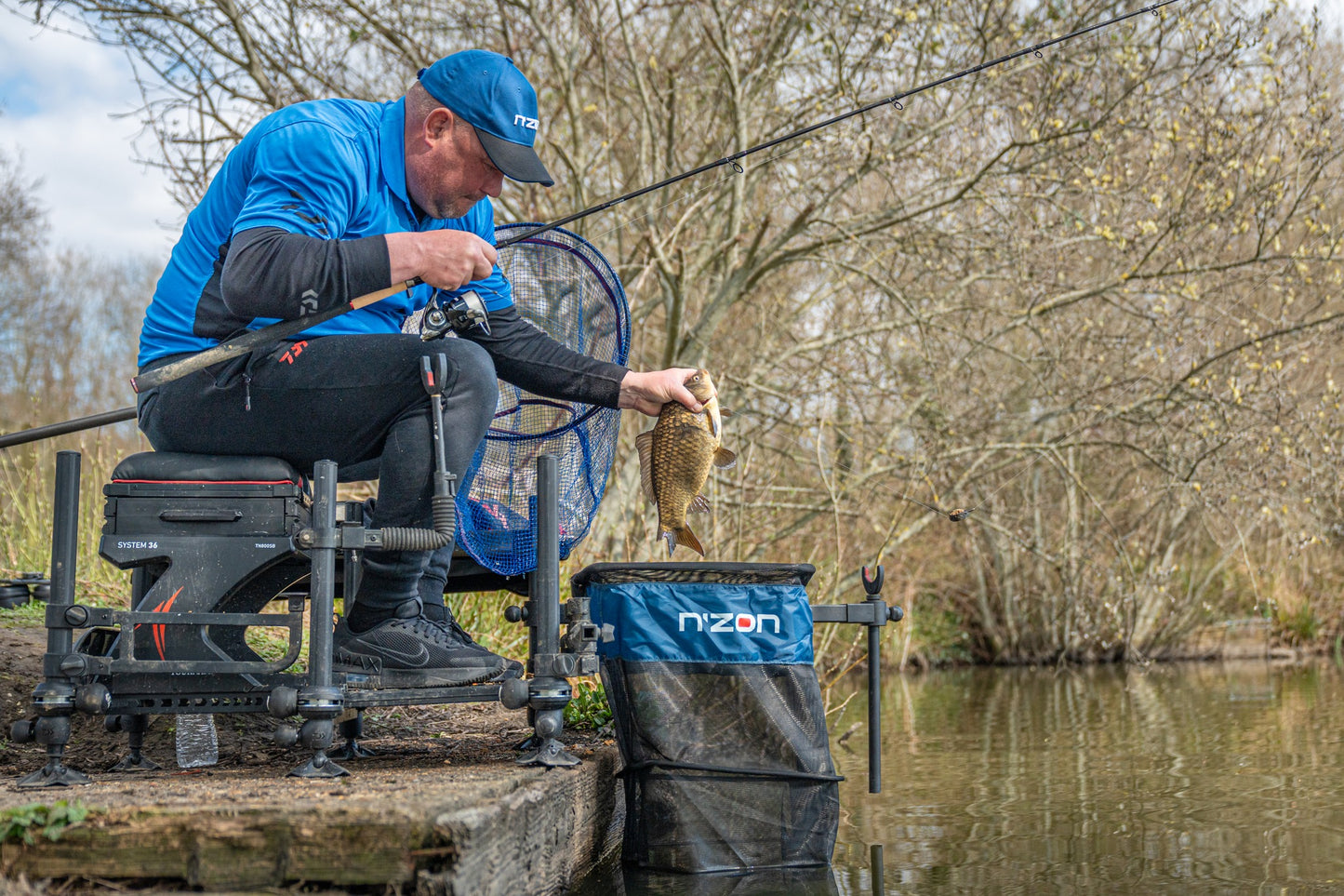 Рибар, който държи риба с преден държач за въдица DAIWA N'ZON COMPACT FRONT ROD REST на водоема.