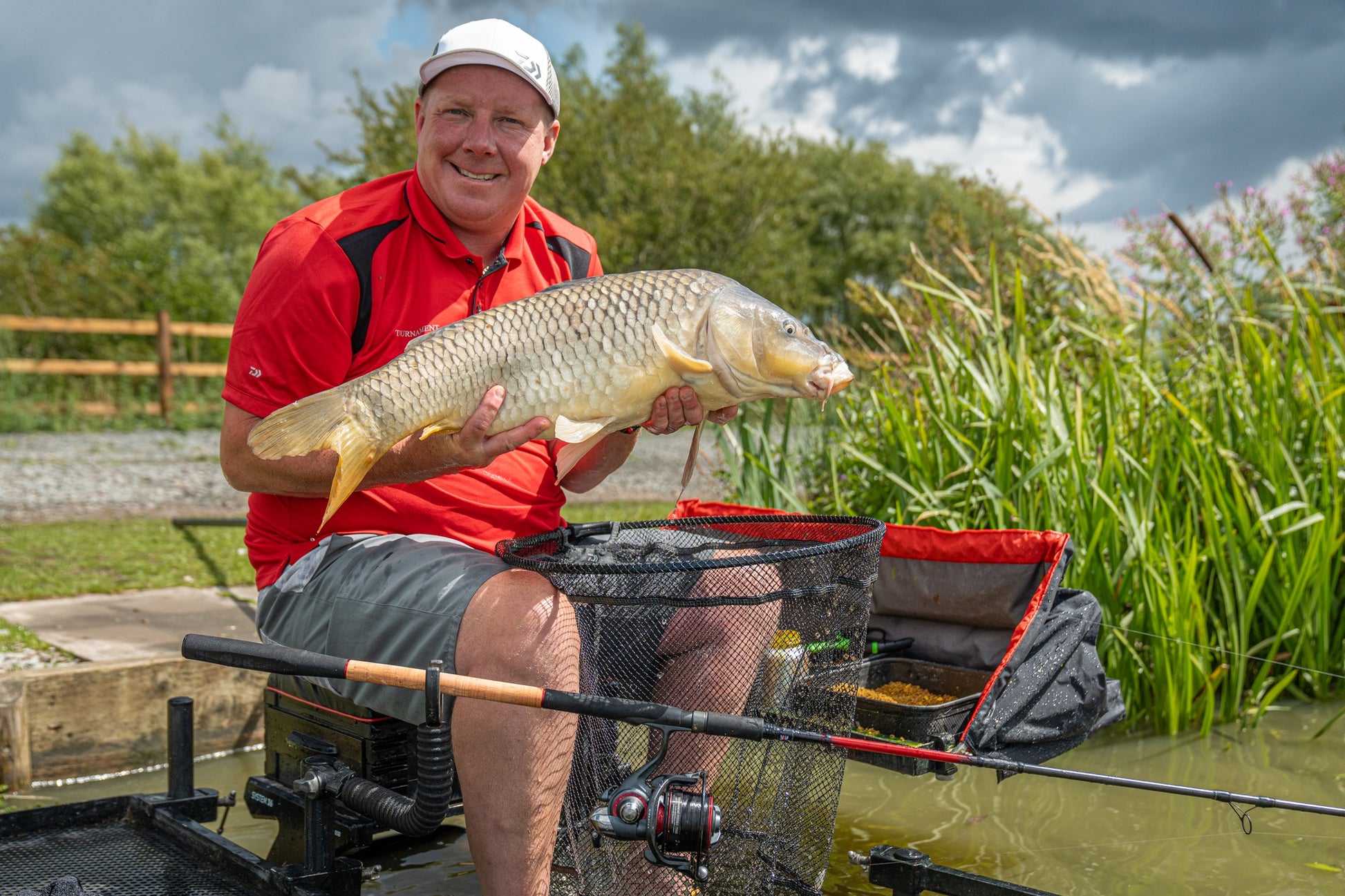 Риболовец с фидер въдици DAIWA TOURNAMENT SLR - New model 2025, държи улавяне на шаран за риболов на водоем.