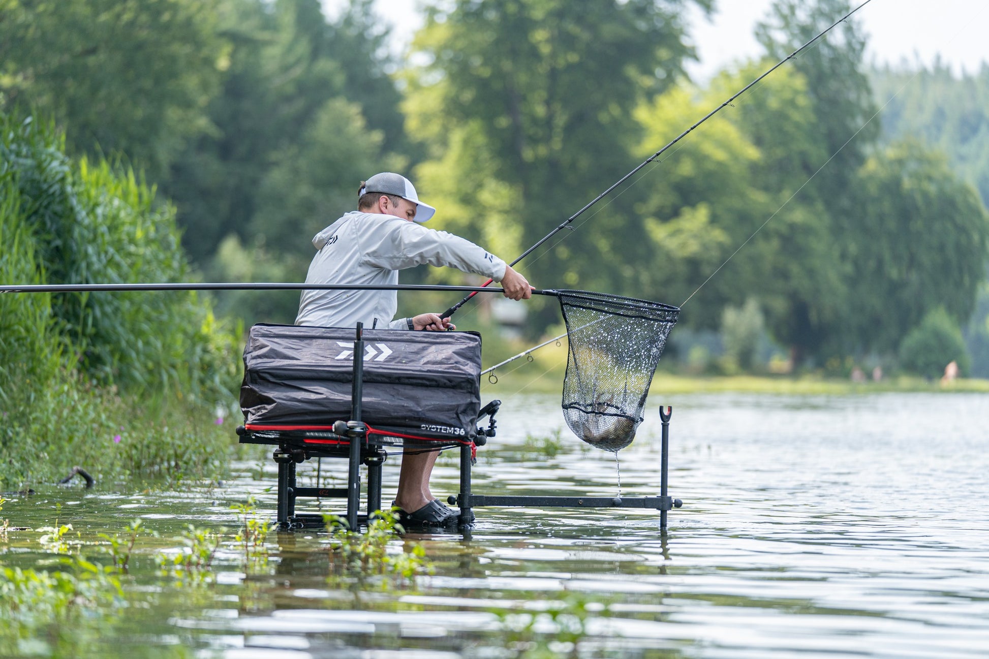 Риболовец с Дръжка за кеп DAIWA 25 AIR LANDING NET HANDLE 4.50m на водоем.