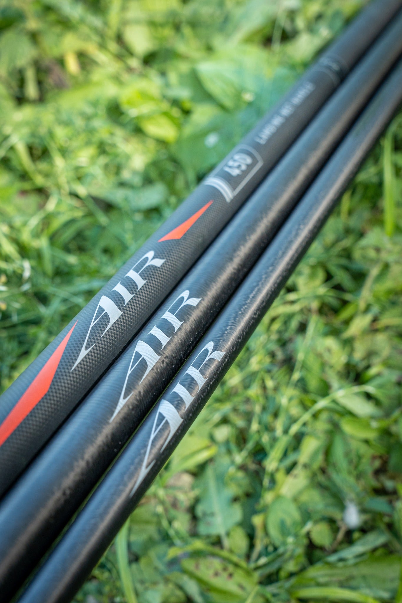 Дръжка за кеп DAIWA 25 AIR LANDING NET HANDLE 4.50m в зелена растителност, идеална за риболов.