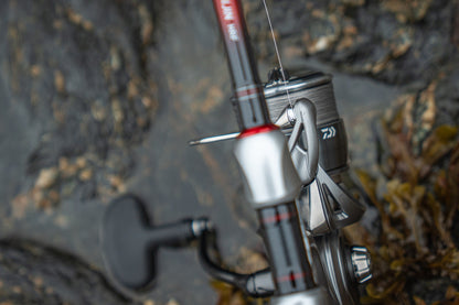 Макара DAIWA 25 CALDIA FC LT на риболовен прът върху скална повърхност, готова за риболов.