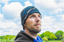 Мъж в зимна шапка PRESTON CELCIUS BEANIE, стоящ на открито сред облаци и зеленина.
