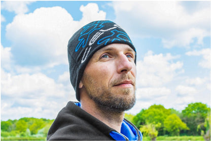 Мъж в зимна шапка PRESTON CELCIUS BEANIE, стоящ на открито сред облаци и зеленина.