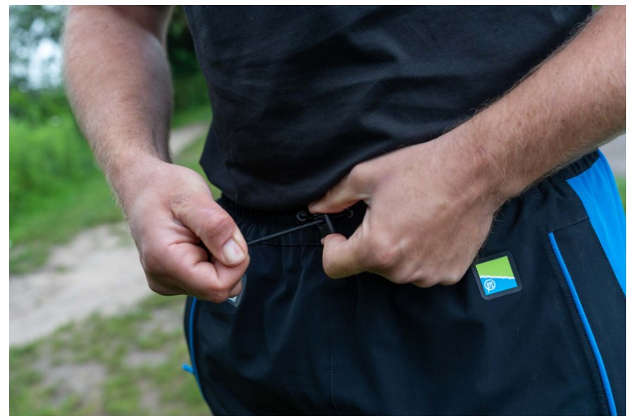 Водоустойчив панталон PRESTON DF ULTRA TROUSERS, затягане на колана от риболовец на открито.