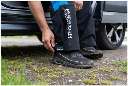 Водоустойчив панталон PRESTON DF ULTRA TROUSERS, удобен за риболов, показан на рибар, обуща и автомобил.
