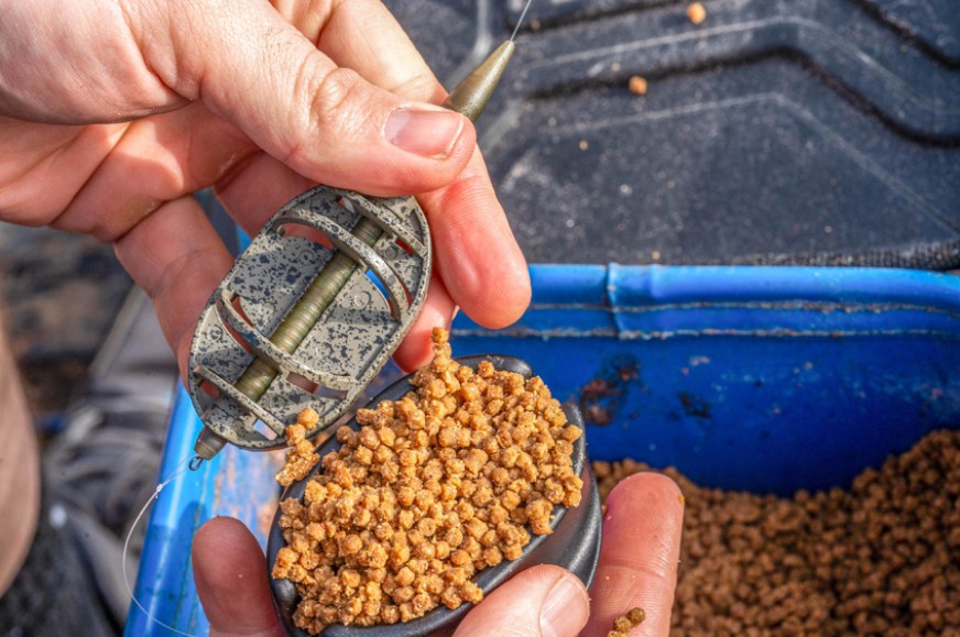 Метод хранилка PRESTON ICS INLINE DURA FLAT METHOD FEEDER - XXL с храна за риба в ръката на рибар.
