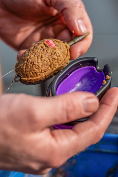 Форма PRESTON QUICK RELEASE METHOD MOULD - XXL с риболовна хранилка и пружинен бутон в ръка.